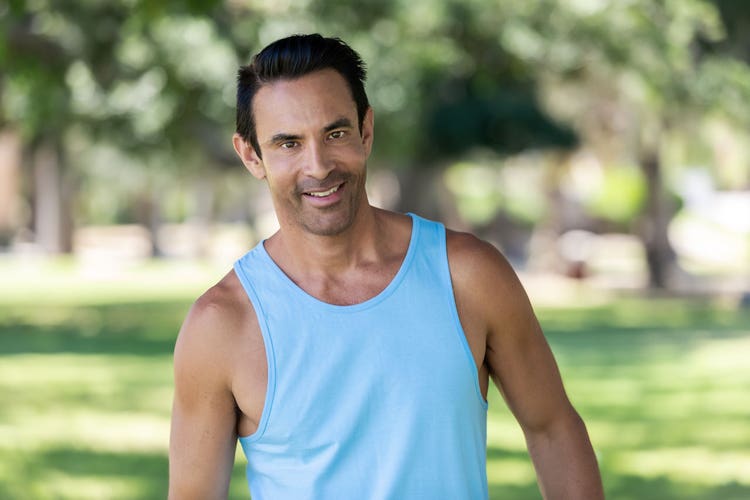 Jorge Cruise stands outside while wearing a light blue tank top