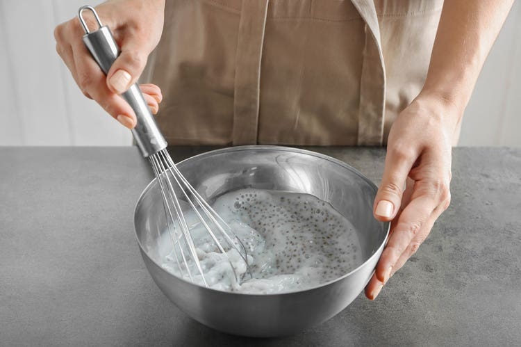 Overhead view of hands whisking a metal bowl full of chia seed pudding