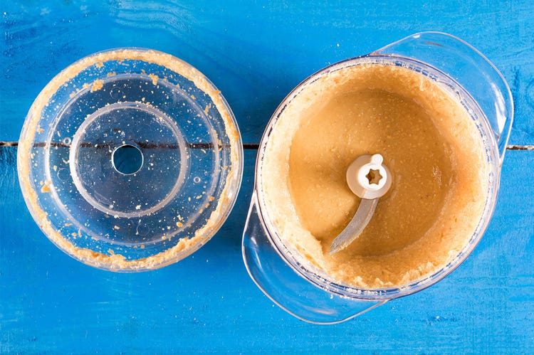 Freshly pureed nut butten in a blender container on a blue table