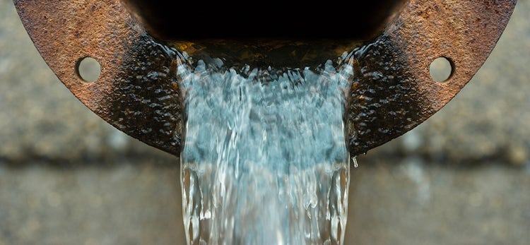 A closeup of water pouring out of a metal drain
