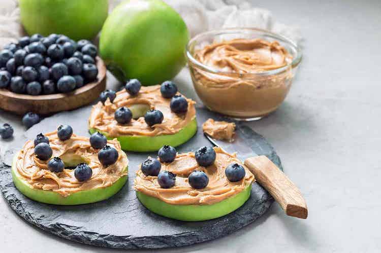 A plate of green apple slices topped with a layer of nut butter and fresh blueberries