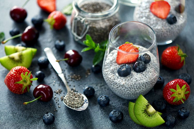 a spread of chia seed pudding glasses topped with berries with cut fruit scattered around the counter