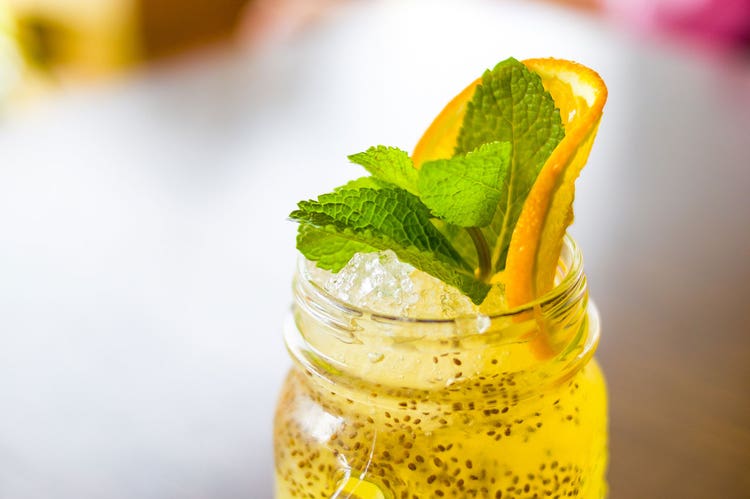 A mason jar is filled with transparent orange chia seed pudding drink, topped off with an orange and mint garnish
