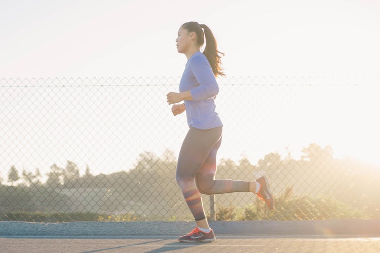 A runner with a long ponytail wearing exercise clothing jogs past a chainlink fence