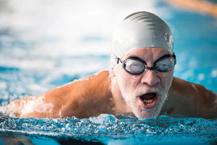 man swimming in pool with swimcap and goggles
