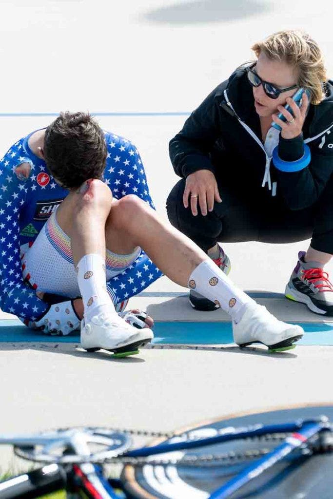 Phil Gaimon crouched on the ground next to his bike and a race official on the track after his crash