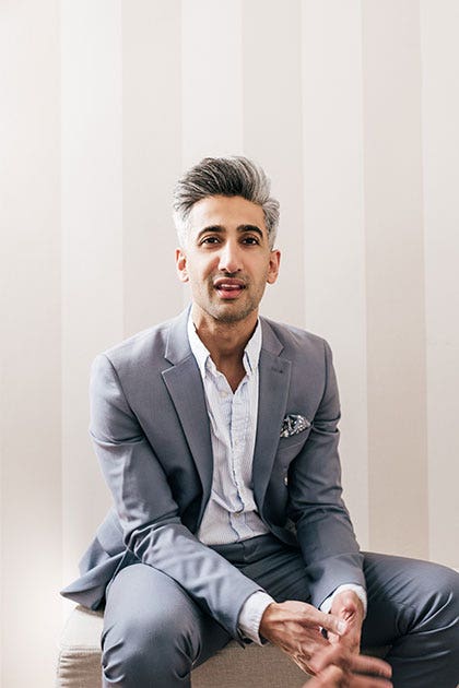 Tan wearing a grey suit and sitting in front of a beige striped wall