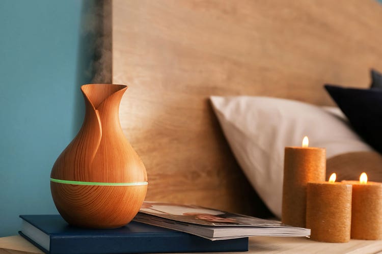 An assortment of candles and a diffuser on a bedstand