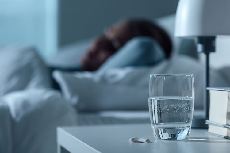 A glass of water and pills on a bedside table next to a person sleeping